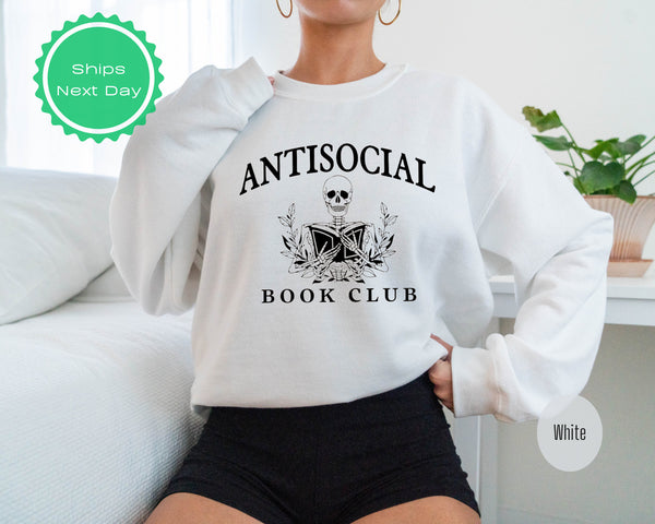 a woman sitting on a couch wearing a book club sweatshirt